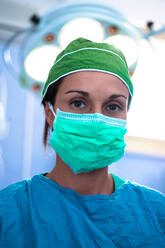 Kopf-Schulter-Porträt einer Chirurgin in OP-Kleidung und Mundschutz, die in die Kamera schaut. - CUF55925