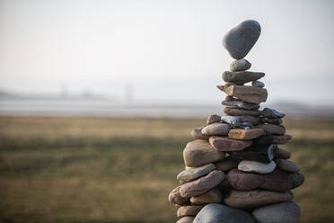 Ein Turm aus unterschiedlich großen Steinen, die zu einem Steinhaufen aufgeschichtet sind, wobei der oberste Stein auf einer Spitze balanciert. - CUF55957