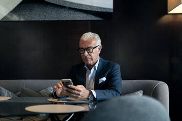 Senior businessman sitting in hotel table using smartphone touchscreen - CUF55983