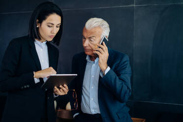 Geschäftsmann und Frau schauen auf ein digitales Tablet und führen einen Smartphone-Anruf im Sitzungssaal - CUF55993