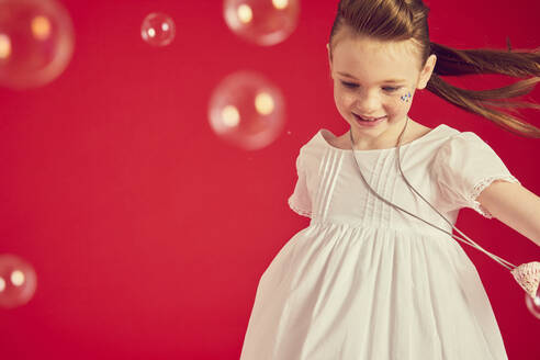 Porträt eines brünetten Mädchens im romantischen weißen Kleid auf rotem Hintergrund, umgeben von Seifenblasen. - CUF56001
