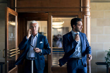 Two businessmen leaving hotel lobby, using mobile phones. - CUF56081