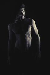 Handsome shirtless man with long hair standing in dark room and looking away - ADSF01261