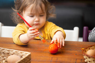 Adorable Kleinkind Mädchen mit Pinsel zu malen Osterei, während am Tisch sitzen - ADSF01280