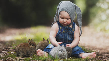 Niedliches kleines Kind mit grauem Hut sitzt mit Hasen im Park. - ADSF01289