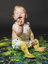 Adorable schmutzigen kleinen Jungen sitzen und spielen mit gelben und blauen Farbe auf dunklem Hintergrund. - ADSF01298