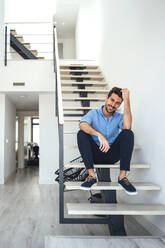 Glücklicher Mann sitzt auf einer schwebenden Treppe in einem modernen Penthouse - EHF00542