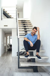 Happy man sitting on floating stairs in modern penthouse - EHF00542