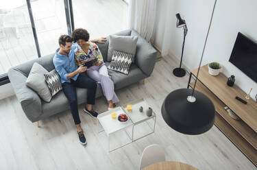 Multi-ethnic couple using digital tablet while sitting on sofa in living room of modern penthouse - EHF00545