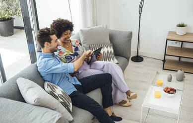 Glückliches Paar, das ein digitales Tablet benutzt, während es auf dem Sofa im Penthouse sitzt - EHF00546