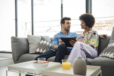Ein multiethnisches Paar benutzt ein digitales Tablet, während es auf dem Sofa in einem modernen Penthouse sitzt - EHF00549