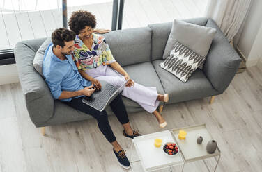 Ein multiethnisches Paar benutzt einen Laptop, während es auf dem Sofa im Wohnzimmer eines Penthouses sitzt - EHF00554