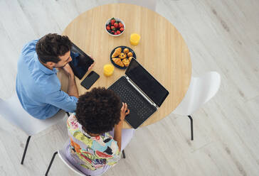 Happy couple using laptop and digital tablet at dining table in penthouse - EHF00555