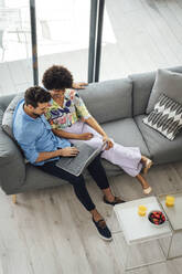 Multiethnisches Paar, das einen Laptop benutzt, während es auf dem Sofa im Penthouse sitzt - EHF00557