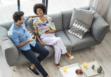 Glückliches multiethnisches Paar mit Smartphones in der Hand, während es auf dem Sofa im Penthouse sitzt - EHF00561