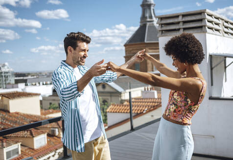 Glückliches multiethnisches Paar tanzt auf der Penthouse-Terrasse an einem sonnigen Tag - EHF00612