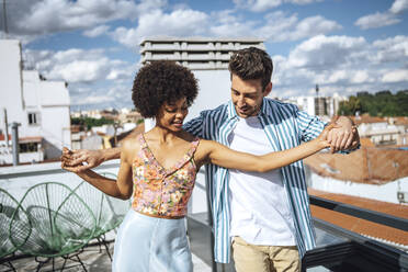 Multi-ethnic couple dancing on penthouse patio during sunny day - EHF00614