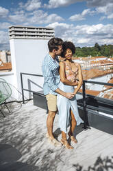 Romantisches multiethnisches Paar umarmt sich auf der Penthouse-Terrasse an einem sonnigen Tag - EHF00618