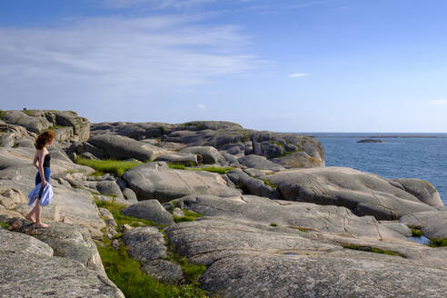 Teenage girl standing alone on rocky coast - LBF03165