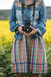 Crop unerkennbar Dame in farbigen Kleid und Jeansjacke hält Foto-Gerät in der Natur - ADSF01444