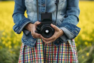 Crop unrecognizable lady in colored dress and jeans jacket holding photo device in nature - ADSF01445