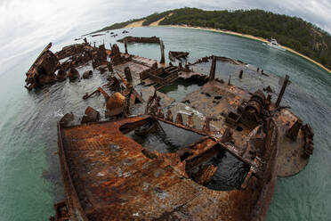 From above wide angle rusty ship wrecked at green shore in blue ocean water - ADSF01460