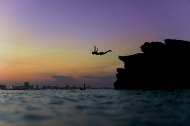 Seitenansicht der Silhouette einer Person, die vom Stein aus ins Meerwasser taucht - ADSF01463