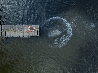 Luftaufnahme eines Mannes, der am Rande eines Stegs am Seeufer steht - KNTF04988