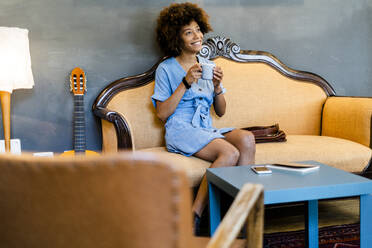 Nachdenkliche Frau hält Kaffeetasse, während sie auf dem Sofa in einem modernen Café sitzt - GIOF08504