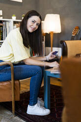 Schöne junge Frau, die eine Kreditkarte hält, während sie einen Laptop in einem Café benutzt - GIOF08513