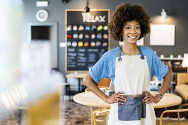 Confident female owner standing with hands on hips at coffee shop - GIOF08532