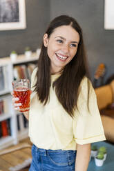 Cheerful young woman holding glass of juice in coffee shop - GIOF08537