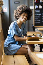 Happy young woman writing in book at table in coffee shop - GIOF08541