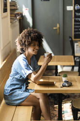 Nachdenkliche Frau, die eine Kaffeetasse hält, während sie am Tisch in einem Café sitzt - GIOF08542