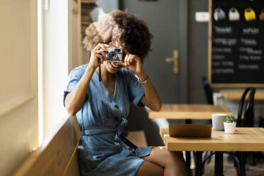 Glückliche junge Frau, die eine Digitalkamera benutzt, während sie in einem Café sitzt - GIOF08543