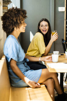 Fröhliche Frau hält ein Getränk in der Hand und schaut einem Freund im Café zu - GIOF08548