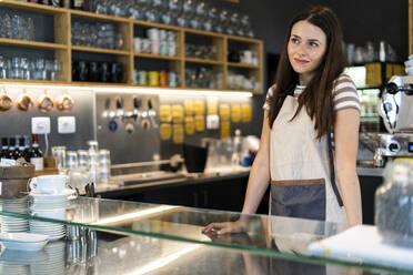 Thoughtful female owner standing at counter in coffee shop - GIOF08552