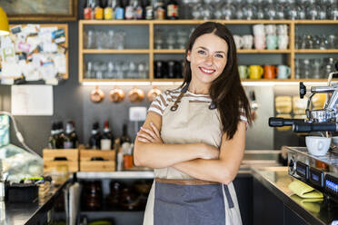 Happy female owner standing arms crossed in coffee shop - GIOF08561