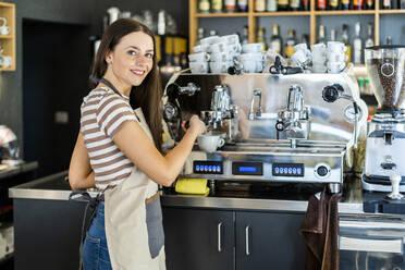 Glückliche weibliche Barista mit Kaffeemaschine im Café - GIOF08562