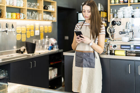 Junge Frau, die in einem Café steht und ihr Smartphone benutzt - GIOF08563