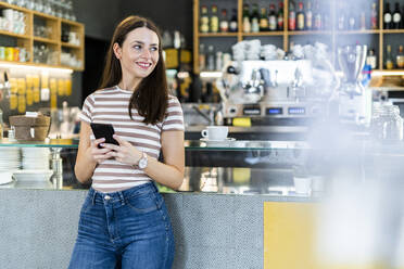 Thoughtful woman holding smart phone while standing at coffee shop - GIOF08567