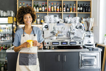 Glückliche weibliche Barista hält Kaffeebecher im Café - GIOF08568