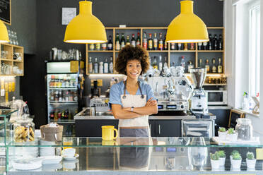 Glückliche weibliche Barista steht mit verschränkten Armen in einem Café - GIOF08569