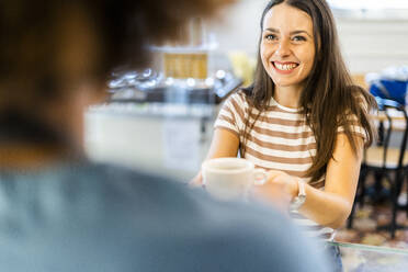 Happy female owner selling coffee to woman in cafe - GIOF08572