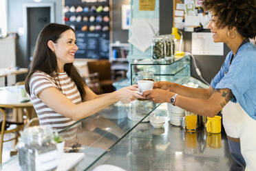 Glücklicher Besitzer verkauft Kaffee an junge Frau in Café - GIOF08573
