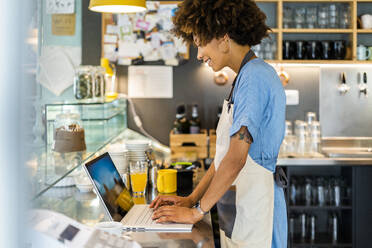 Weiblicher Besitzer benutzt Laptop am Tresen eines Cafés - GIOF08575