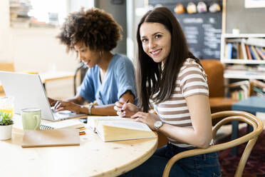 Glückliche Freundinnen studieren mit Laptop am Tisch in einem Café - GIOF08582