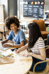 Glückliche Frauen studieren mit Laptop am Tisch in einem Café - GIOF08583