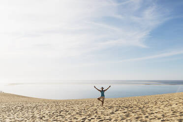 Frau schaut auf den Atlantik, während sie an einem sonnigen Tag am Strand trainiert, Düne von Pilat, Nouvelle-Aquitaine, Frankreich - GWF06625