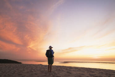 Älterer Mann mit Rucksack schaut auf den Atlantik gegen den Himmel während des Sonnenuntergangs, Düne von Pilat, Nouvelle-Aquitaine, Frankreich - GWF06639